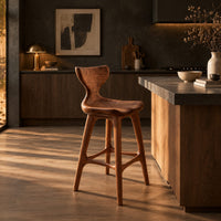 Bar stool with a winged backrest and a dished saddle seat in a dark kitchen at golden hour