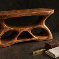 Corner detail of vanity with a flowing oval top and a sculpted base pierced by smooth openings beside wood, brass and linen samples