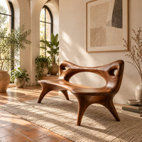 Bench with an open loop backrest and four splayed legs in a bright entryway with arched windows and plants