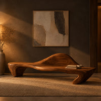 Long wooden bench with a raised wave shaped backrest and curved legs in a dark entryway at golden hour