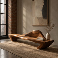 Long wooden bench with a raised wave shaped backrest and curved legs in an industrial loft entryway with exposed brick