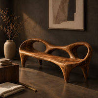 Corner detail of wooden bench with a low backrest cut with two oval openings on tapered legs beside wood, brass and linen samples