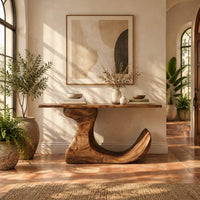 Console table on an off center pedestal with curled foot in a bright entryway with arched windows and plants