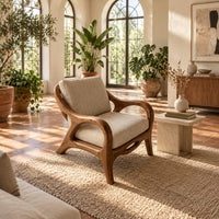 Lounge chair with sweeping arms and an oval cutout seat rail in a bright living room with arched windows and plants