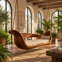 Boat shaped wooden swing with scrolled ends and a long seat cushion in a bright porch with arched windows and plants