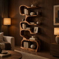 Tall serpentine bookshelf with staggered slab shelves and a loop base in an evening living room with walnut wall paneling