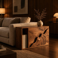 Boxy wood side table with a carved wave front panel and an open slot in an evening living room with walnut wall paneling