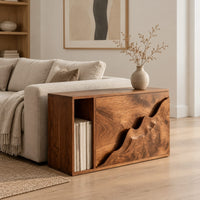 Boxy wood side table with a carved wave front panel and an open slot in a Scandinavian living room with white walls