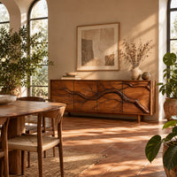 Low sideboard with a carved branch pattern across four front panels in a bright dining room with arched windows and plants