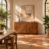 Sideboard with fluted arch carving and rounded ends in a bright dining room with arched windows and plants