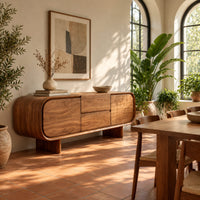 Long sideboard with soft oval ends and a four panel front in a bright dining room with arched windows and plants