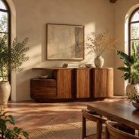 Sideboard with three grooved front panels and a lower block on one end in a bright dining room with arched windows and plants
