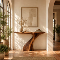 Console table on a single sculpted pedestal that twists up to the top in a bright entryway with arched windows and plants