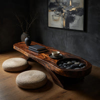 Long dark slab coffee table with a carved bowl in a dark studio against a charcoal wall
