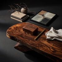 Corner detail of long dark slab coffee table with a carved bowl beside wood, brass and linen samples