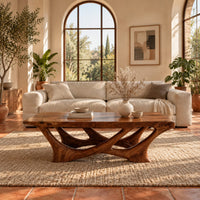 Slab top coffee table on a branching base of crossing curved arms in a bright living room with arched windows and plants
