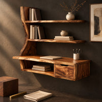 Corner detail of wooden desk with a slab top, wavy side upright, two shelves and a drawer beside wood, brass and linen samples