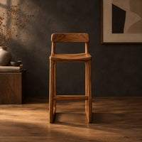 Bar stool with a low back, scooped seat and sled style legs in a dark studio against a charcoal plaster wall