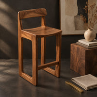 Corner detail of bar stool with a low back, scooped seat and sled style legs beside wood, brass and linen samples