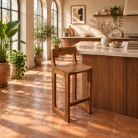 Bar stool with a low back, scooped seat and sled style legs in a bright kitchen with arched windows and plants