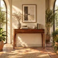 Slim console table with three front panels and tapered legs in a bright entryway with arched windows and plants