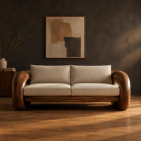 Wood sofa with open ring arms and two wide seat cushions in a dark studio against a charcoal plaster wall