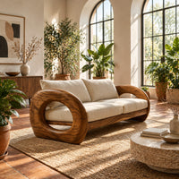 Wood sofa with open ring arms and two wide seat cushions in a bright living room with arched windows and plants