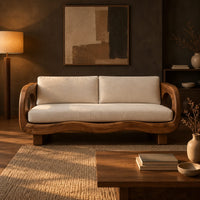 Sofa with oval arm openings, a wavy wooden frame and pale seat cushions in a dark living room at golden hour