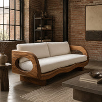 Sofa with oval arm openings, a wavy wooden frame and pale seat cushions in an industrial loft living room with exposed brick