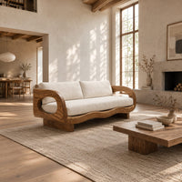Sofa with oval arm openings, a wavy wooden frame and pale seat cushions in a bright open plan living room