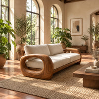 Sofa with thick open loop wooden arms and two seat cushions in a bright living room with arched windows and plants