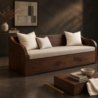 Corner detail of wood sofa with sweeping arms and a deep paneled base beside wood, brass and linen samples