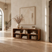 Open console table with soft edges and a long shelf above three cubbies in a bright open plan entryway