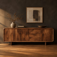 Long low sideboard with soft edges and a drawer stack between doors in a dark studio against a charcoal plaster wall