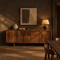 Long low sideboard with soft edges and a drawer stack between doors in a dark dining room at golden hour
