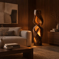 Floor lamp carved as a twisting solid column with glowing cutouts in an evening living room with walnut wall paneling