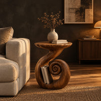 Round side table with a swirling stem and a coiled spiral base in a dark living room at golden hour
