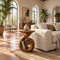 Round side table with a swirling stem and a coiled spiral base in a bright living room with arched windows and plants