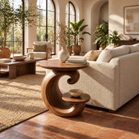 Spiral side table with a curled base and a small lower shelf in a bright living room with arched windows and plants