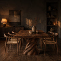 Long dining table on two spiral twisted pedestals with a thick flat top in a dark dining room at golden hour