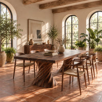 Long dining table on two spiral twisted pedestals with a thick flat top in a bright dining room with arched windows and plants