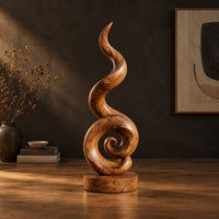 Spiral wood sculpture with a tall flame like swirl and a disc shaped base in a dark studio against a charcoal plaster wall