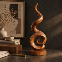 Corner detail of spiral wood sculpture with a tall flame like swirl and a disc shaped base beside wood, brass and linen samples