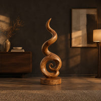 Spiral wood sculpture with a tall flame like swirl and a disc shaped base in a dark living room at golden hour