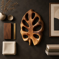 Detail of leaf shaped wall art with open oval cutouts and a short stem beside wood, brass and linen samples