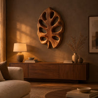 Leaf shaped wall art with open oval cutouts and a short stem above a low console in an evening living room