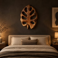 Leaf shaped wall art with open oval cutouts and a short stem above a bed in a dusk lit bedroom