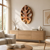Leaf shaped wall art with open oval cutouts and a short stem above a light oak sideboard in daylight