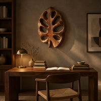 Leaf shaped wall art with open oval cutouts and a short stem above a desk in a dark study corner