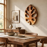 Leaf shaped wall art with open oval cutouts and a short stem beside a dining table in natural light